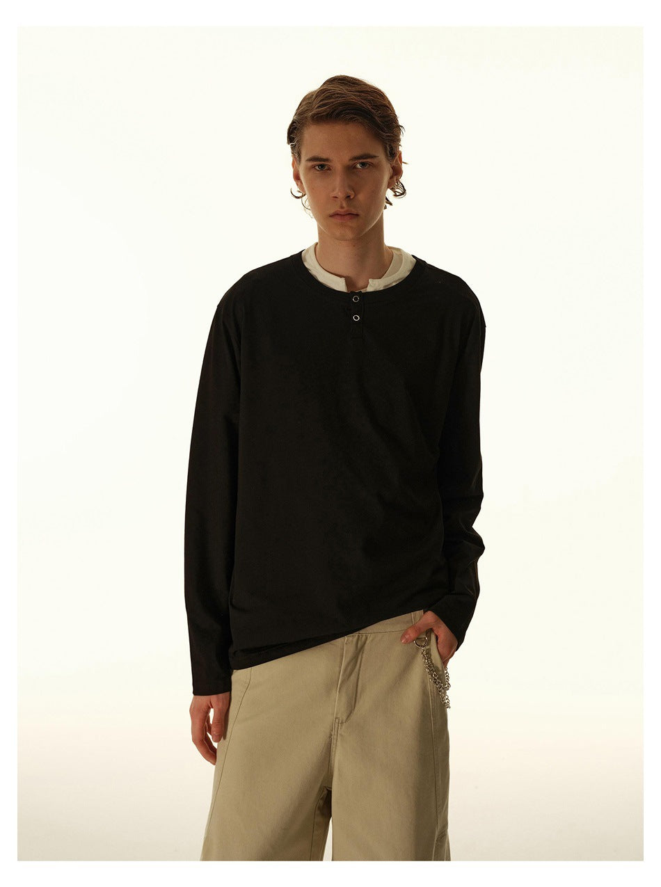 Front view of a model wearing a black long-sleeve henley over a white shirt with beige trousers.