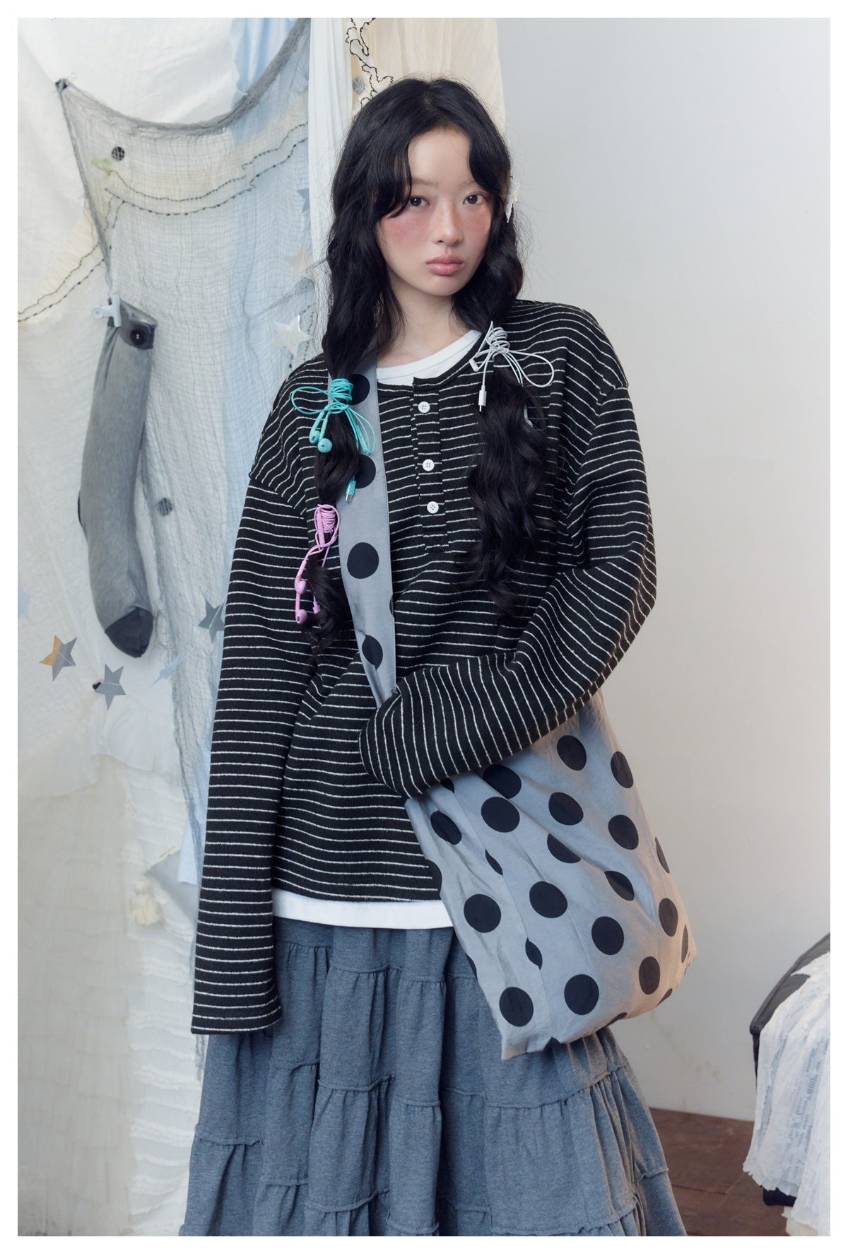 Closer view of a model in a black striped button-front top and charcoal tiered skirt with lace hem, carrying a gray polka-dot