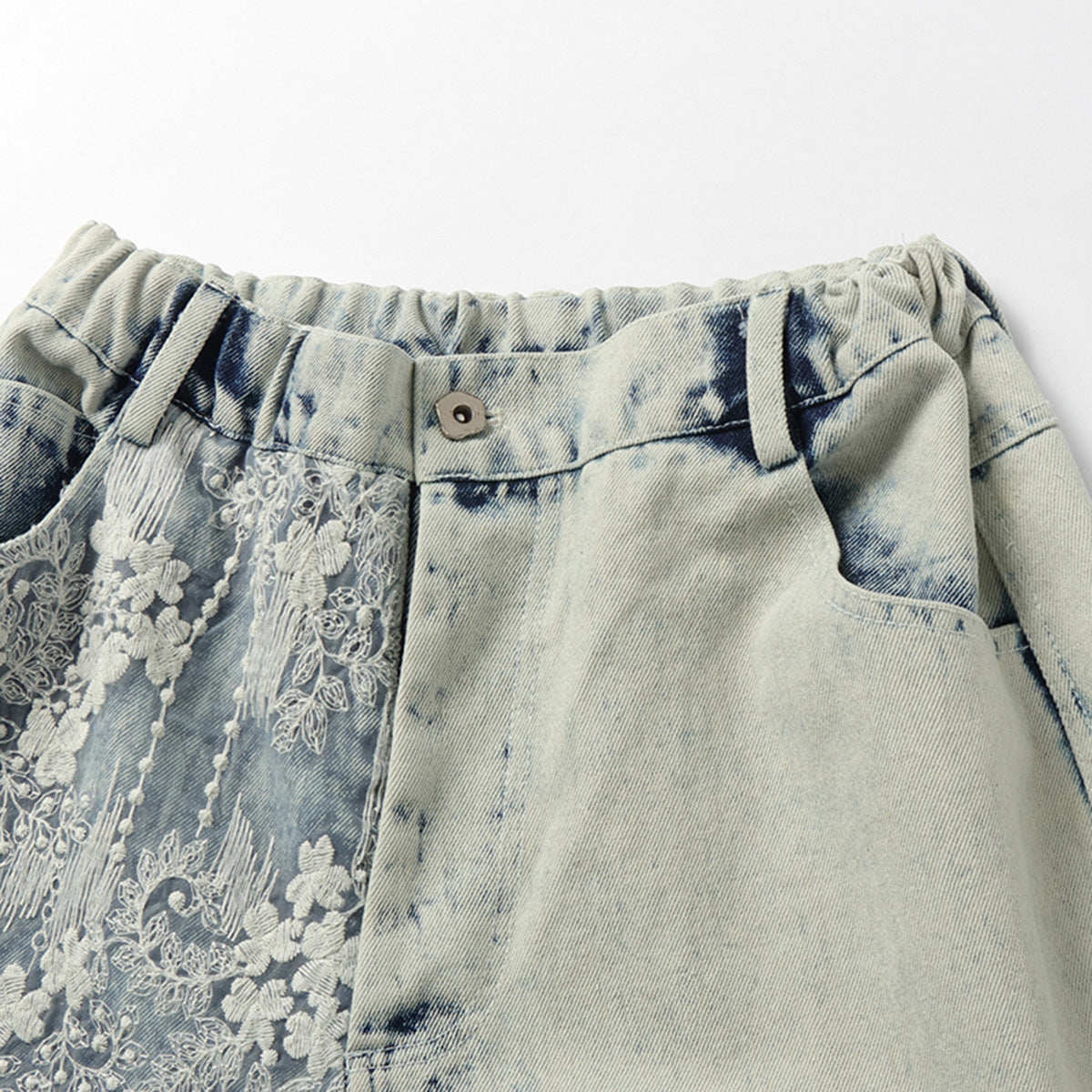 Close-up of pale blue acid-wash denim shorts with a gathered waistband and white floral embroidery on one leg.