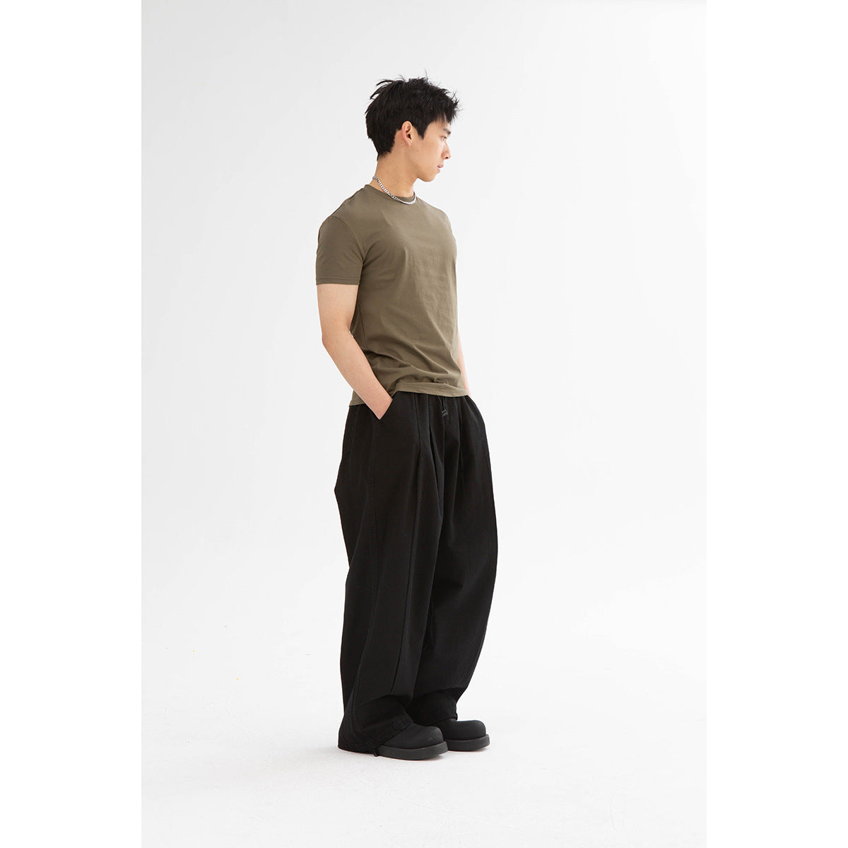 Side-profile model wearing an olive crew-neck T-shirt and loose black trousers.