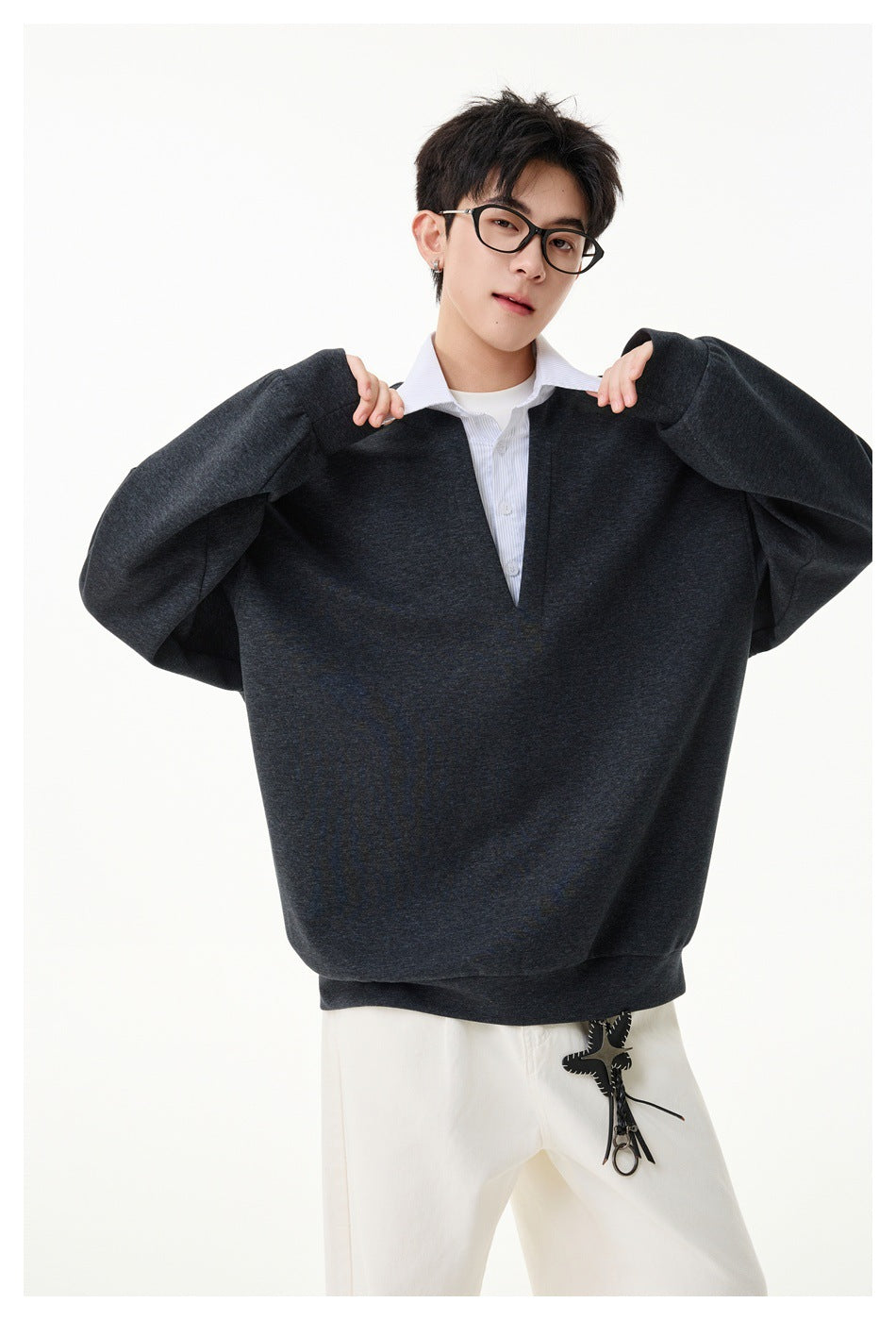 Model wearing a dark gray oversized sweatshirt with a white striped shirt collar and cream pants
