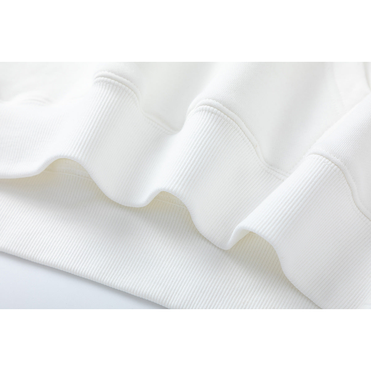 Close-up of white hoodie fabric showing a ribbed cuff or hem and its stitched seam.