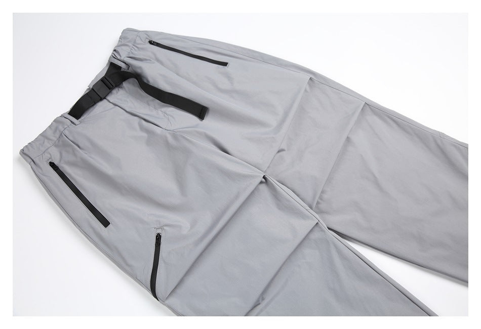 Light gray pants laid diagonally, showing black zip pockets and an adjustable black waist strap.