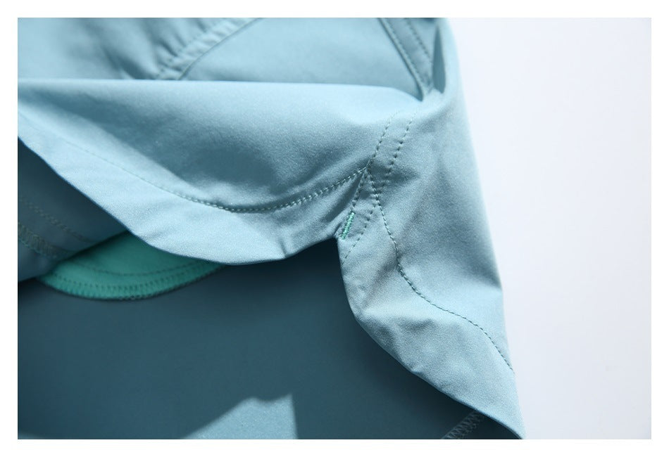 Close-up of stitched seams and a small turquoise bartack near the hem of light blue shorts.