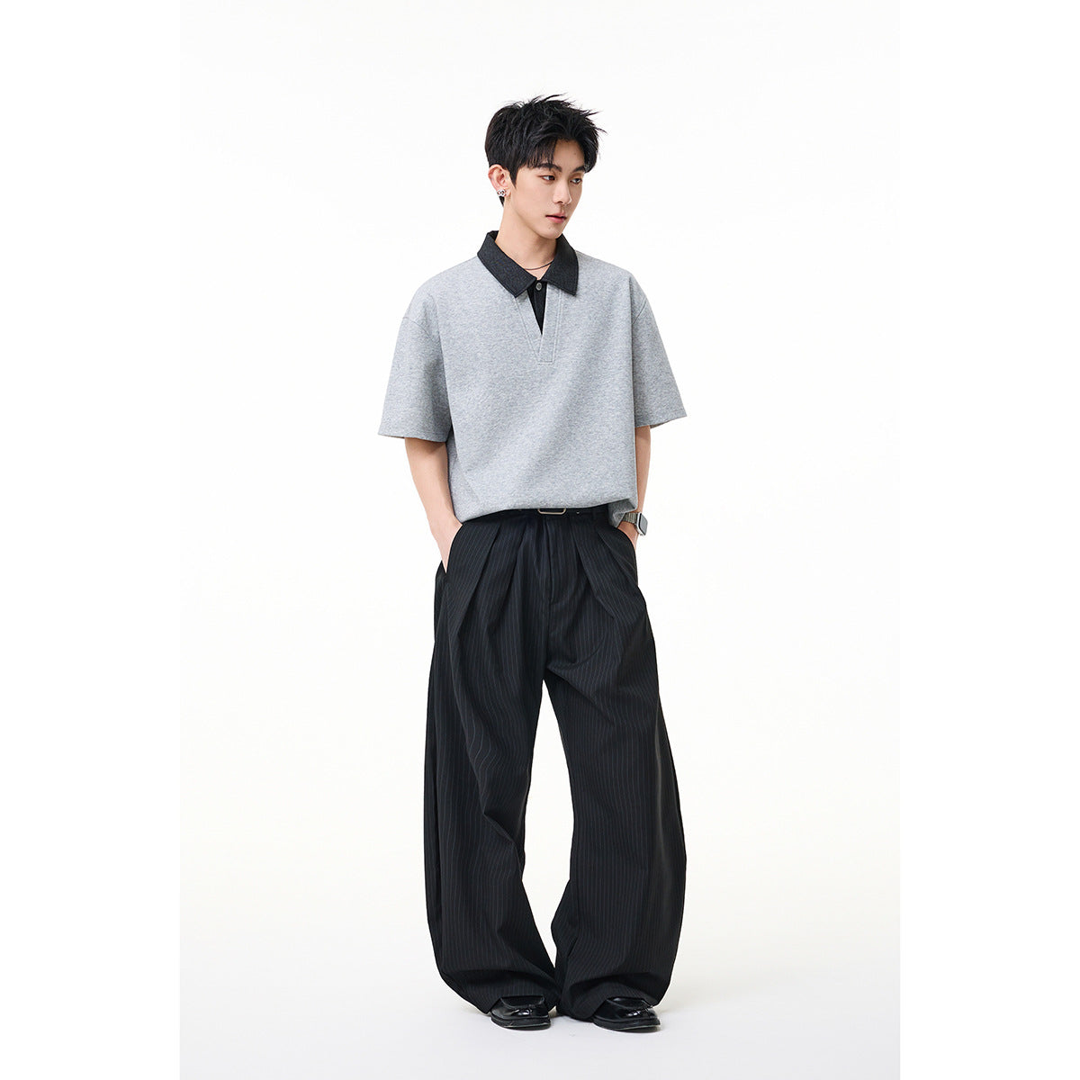 Model wearing a light gray short-sleeve polo-style shirt with a dark collar and loose black pinstripe trousers.