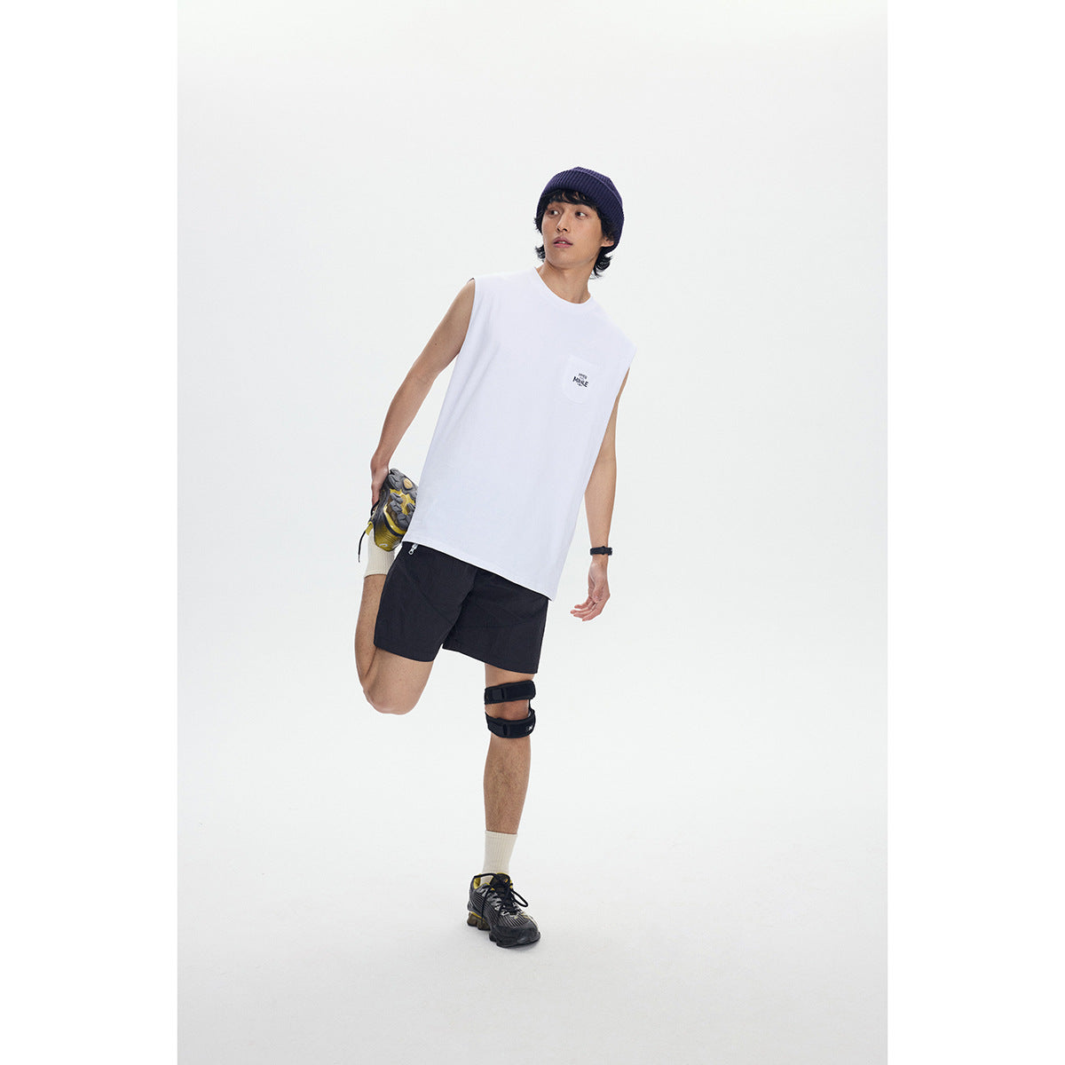 Model wearing a white sleeveless pocket tee and black shorts, shown full length against a white studio background.