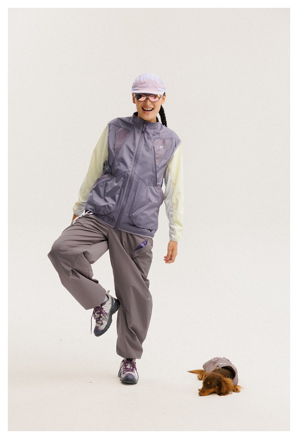 Front view of a model in a lavender-gray utility vest and loose gray-purple pants, with a pale long-sleeve top.
