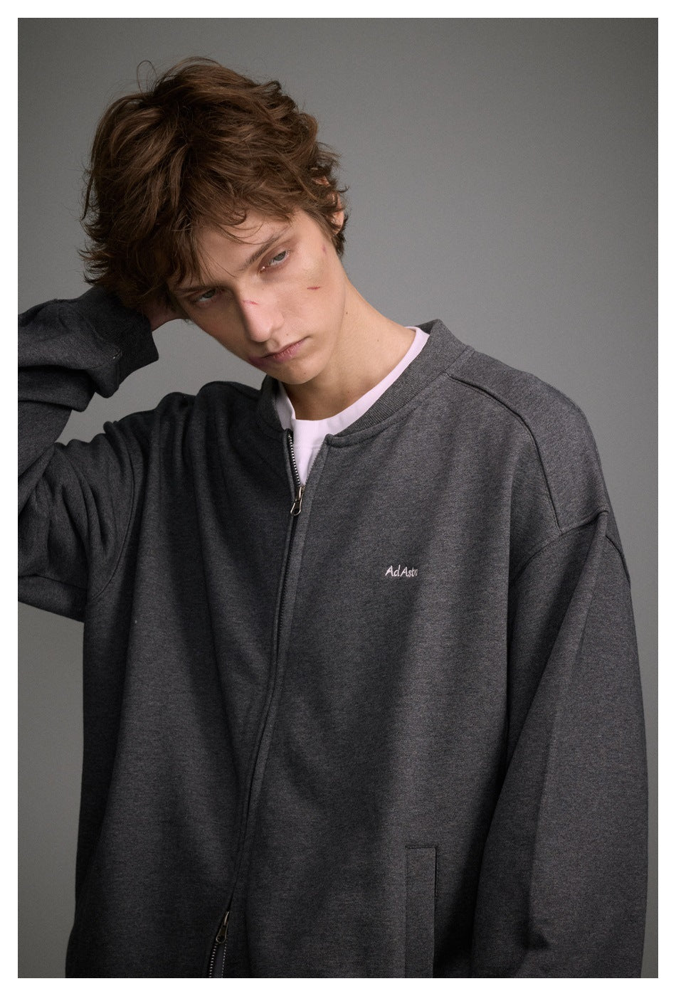 Close view of a model wearing a charcoal gray zip-up jacket with a small embroidered chest logo.