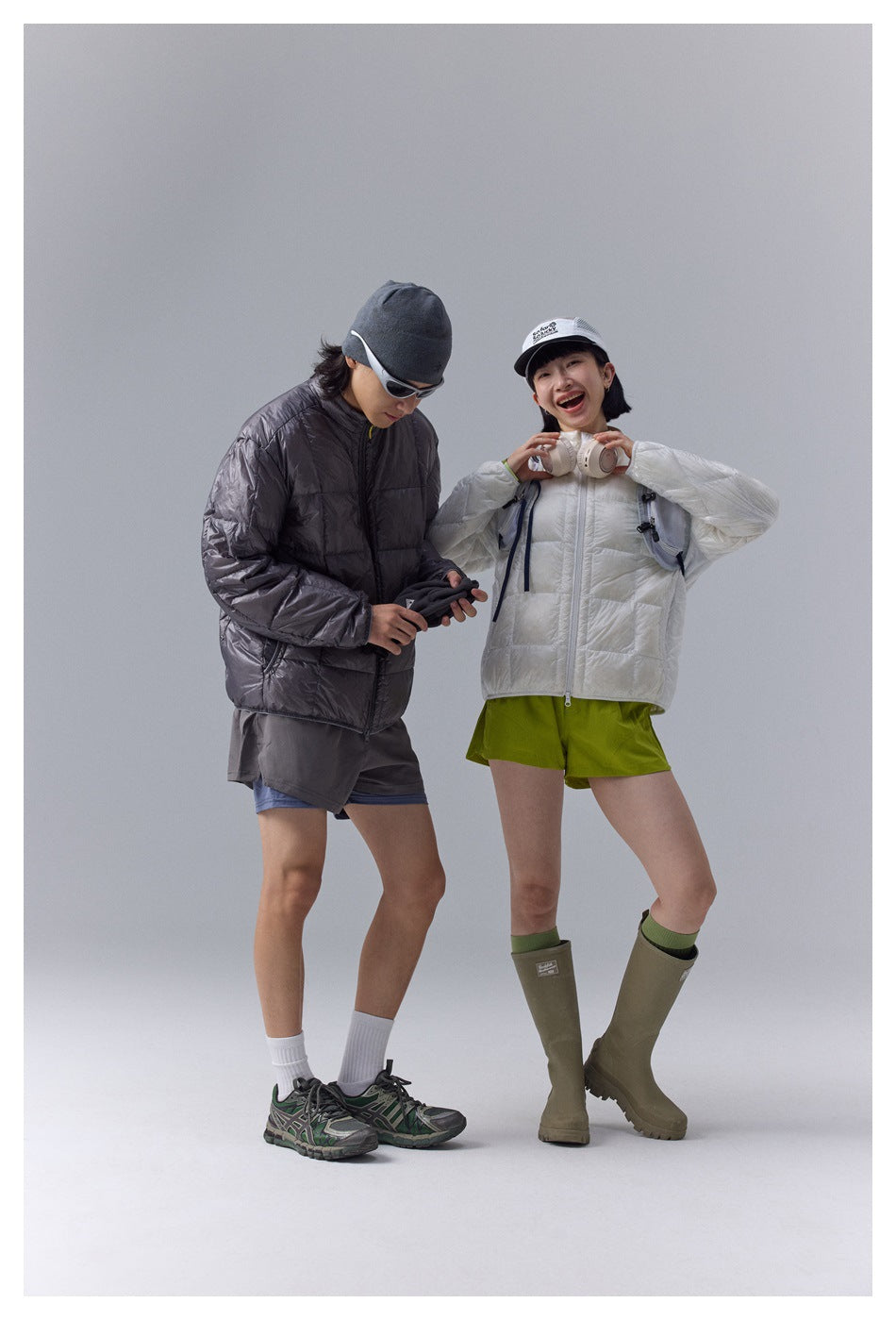 Two models in white and charcoal quilted zip jackets; the woman adjusts headphones around her neck.