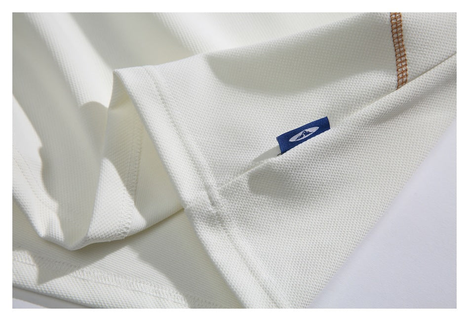 Close-up of white textured garment fabric, tan stitching, and a small blue sewn-in tag.