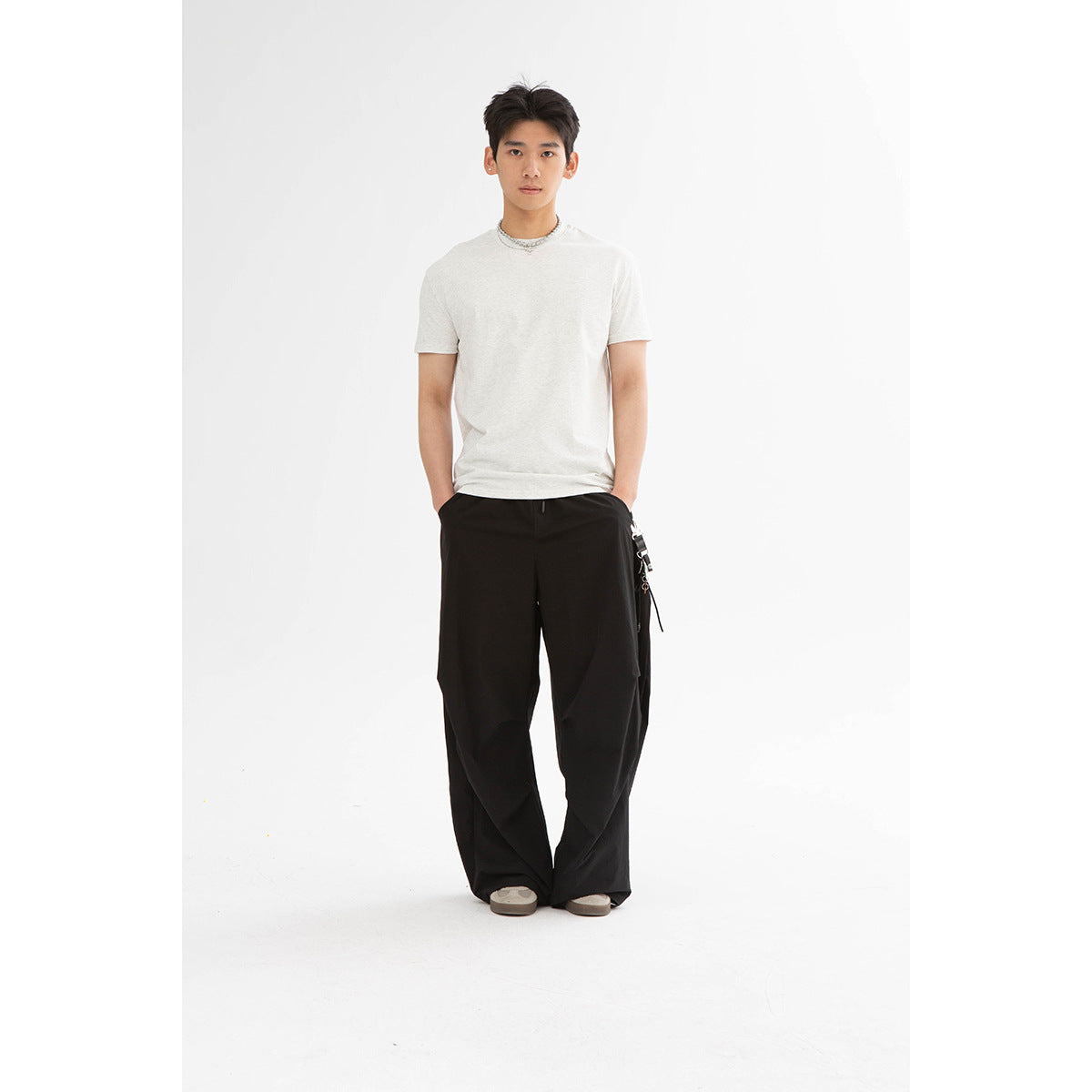Model wearing an off-white crew-neck T-shirt with loose black trousers, shown full-length from the front.