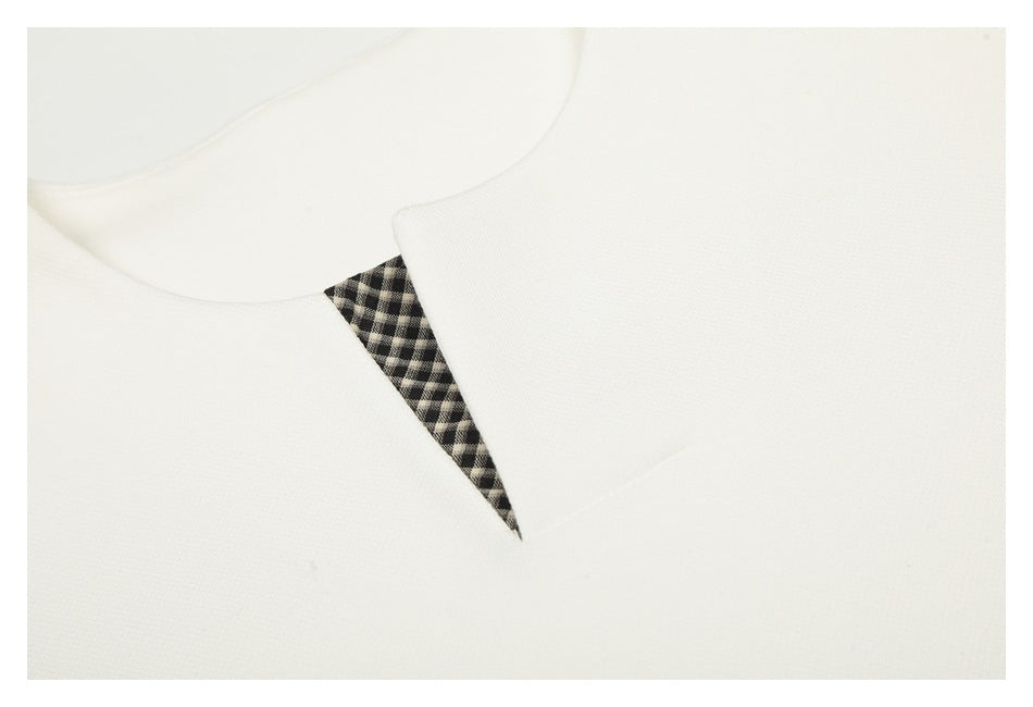 Close-up of a white garment's rounded collar with a black-and-white checked triangular insert.