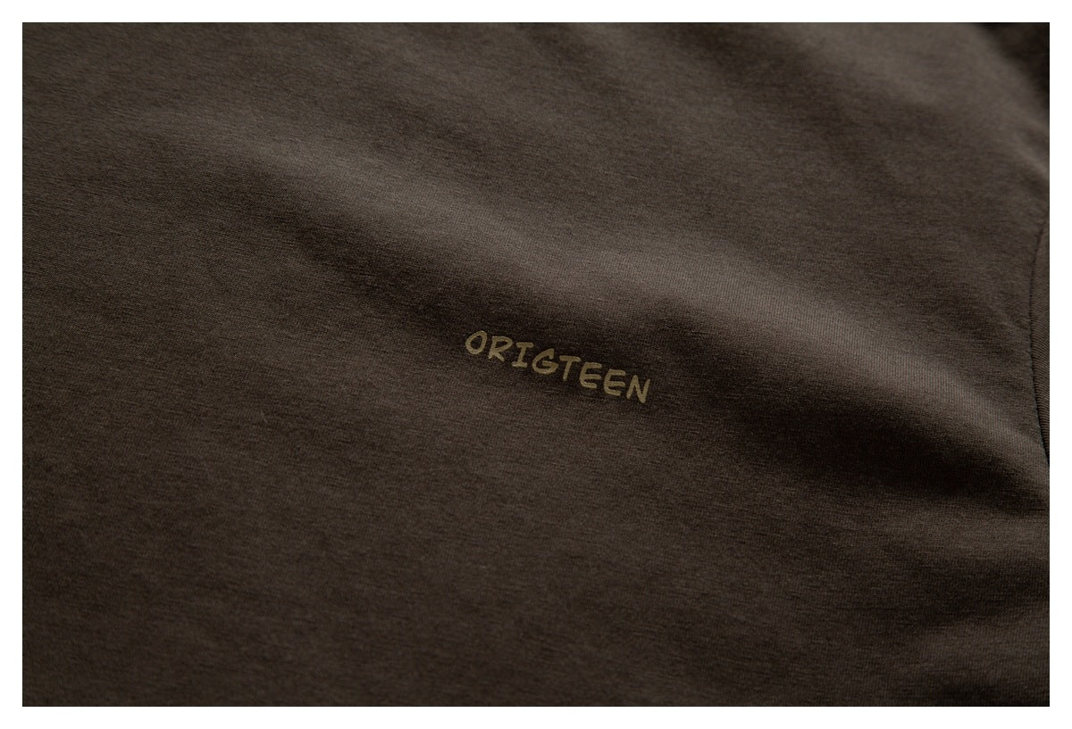 Close-up of a small tan ORIGTEEN print on dark brown fabric.