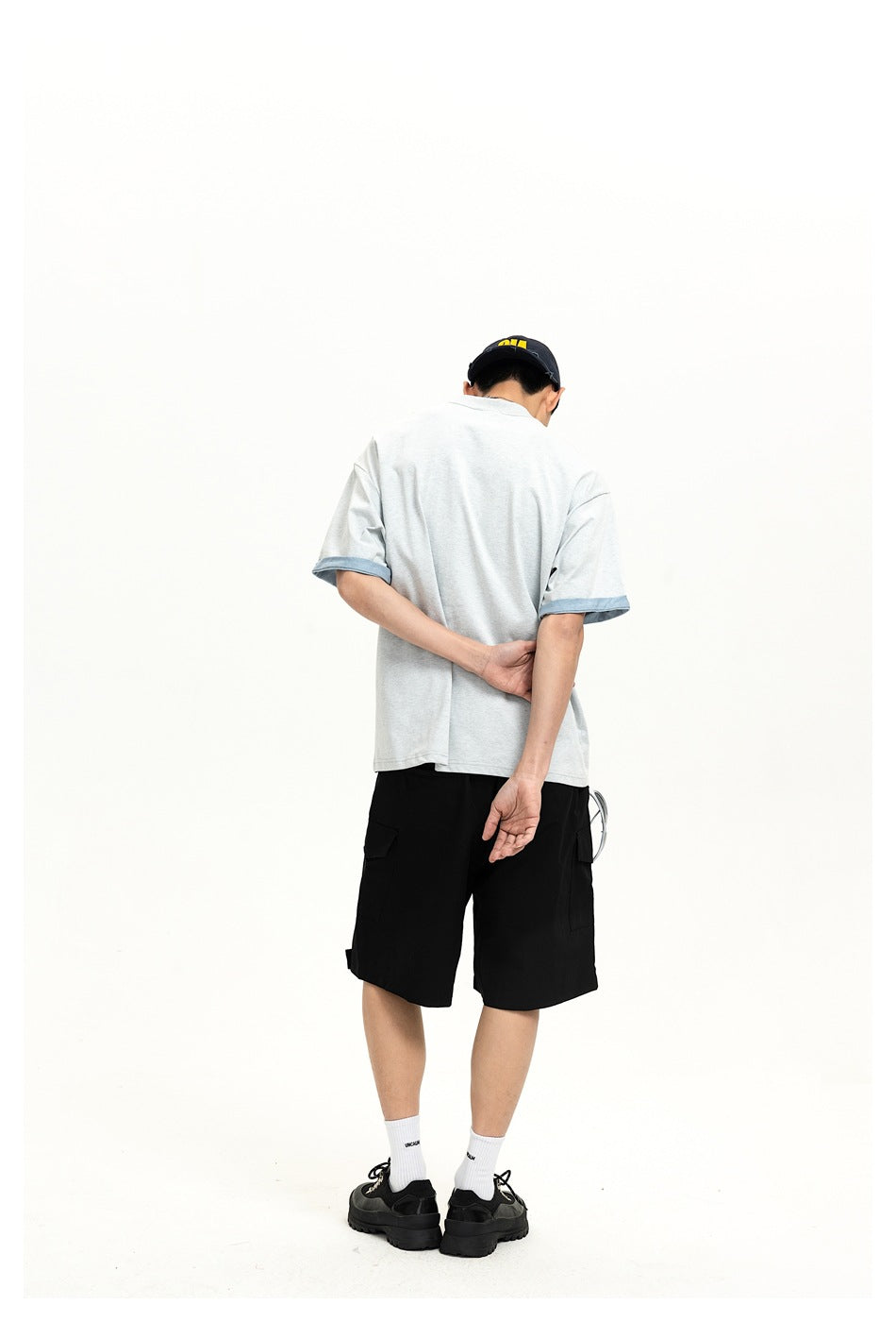 Back view of a model wearing a light gray T-shirt with blue sleeve trim and black cargo shorts.
