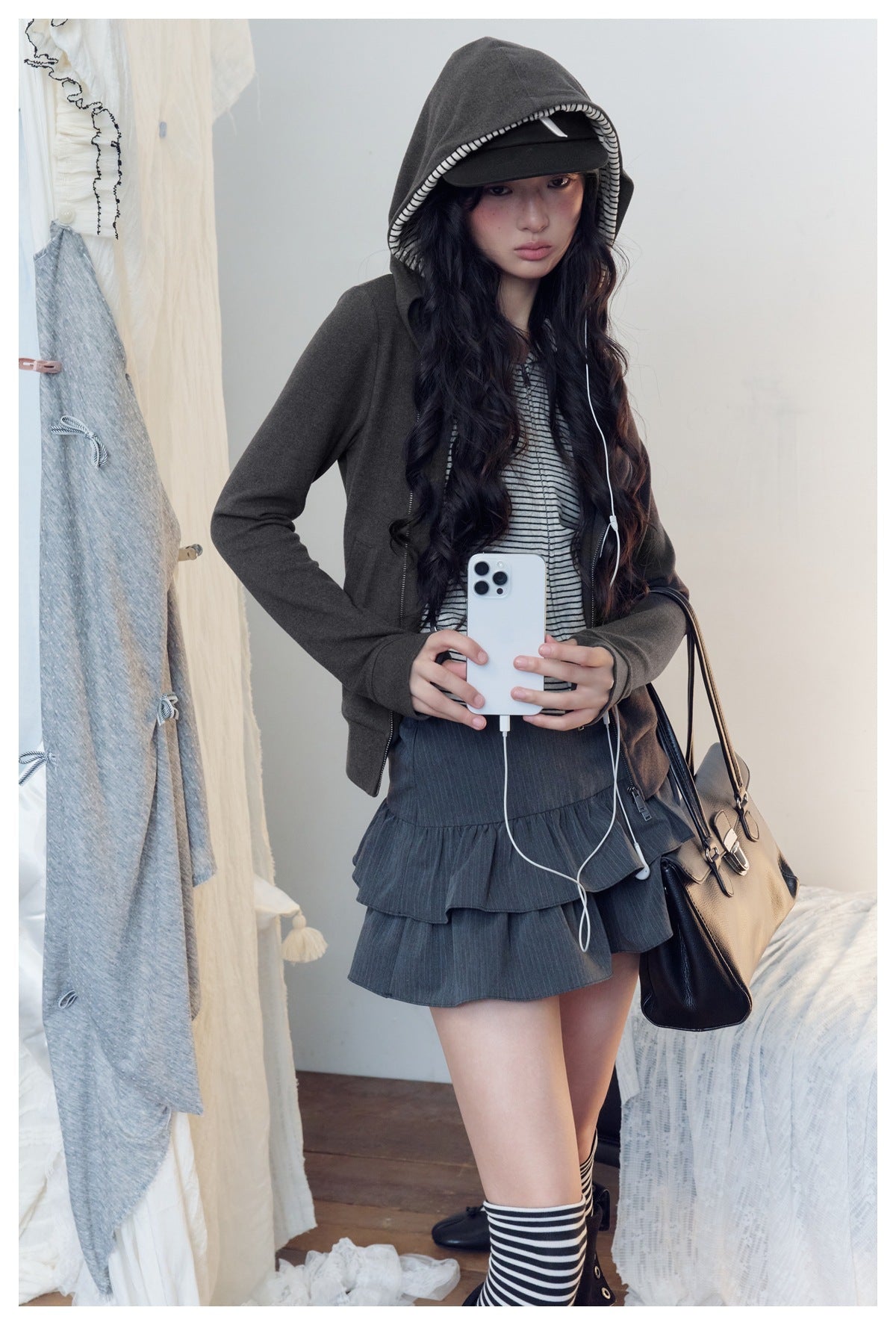 Model wears a charcoal hooded jacket with striped lining over a striped top and tiered dark skirt.