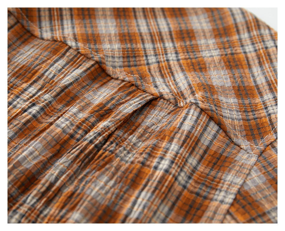 Close-up of a stitched seam joining sections of orange, gray, and cream plaid fabric.