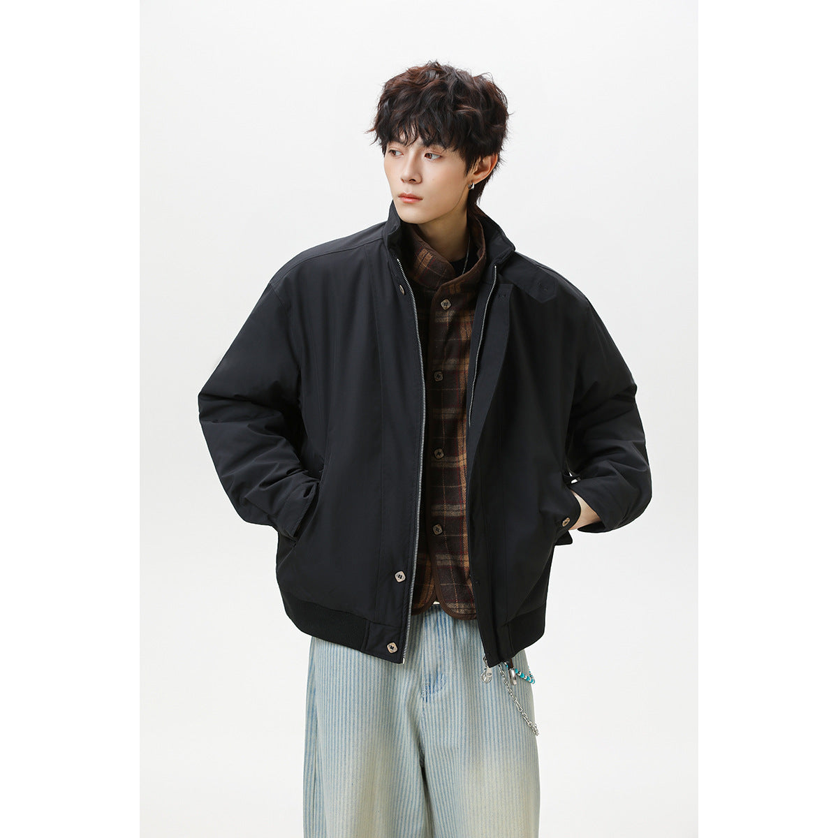 Model wearing an open black zip-front jacket over a brown plaid shirt and pale blue striped trousers.