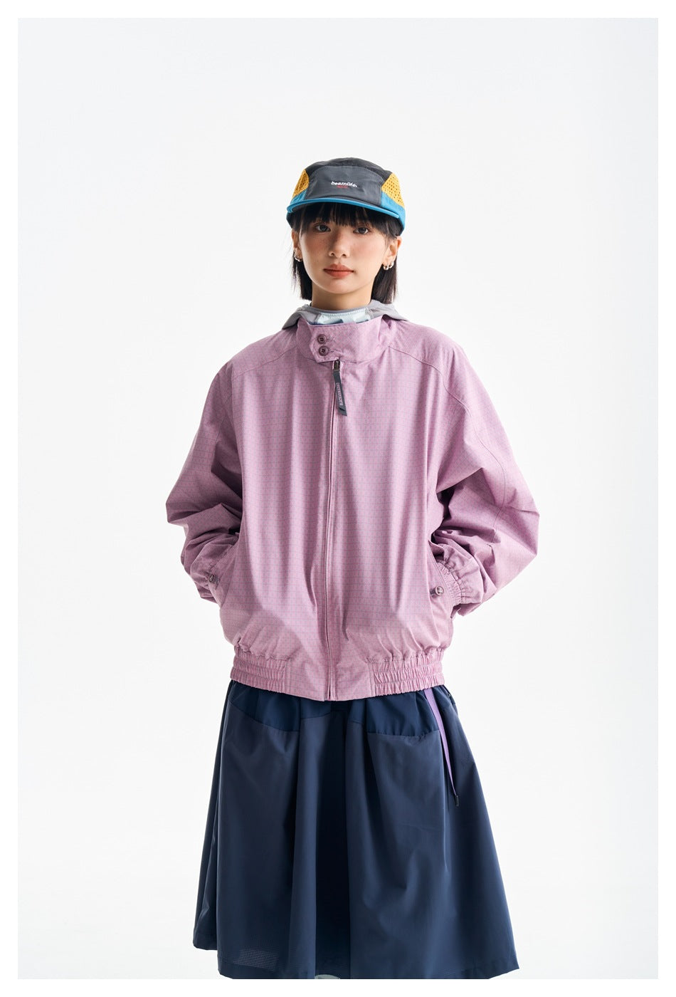 Front view of a model wearing a pink zip jacket with a stand collar and a navy skirt.