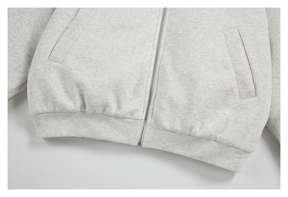 Close-up of the light gray hoodie’s front zipper, angled welt pockets, and ribbed hem.