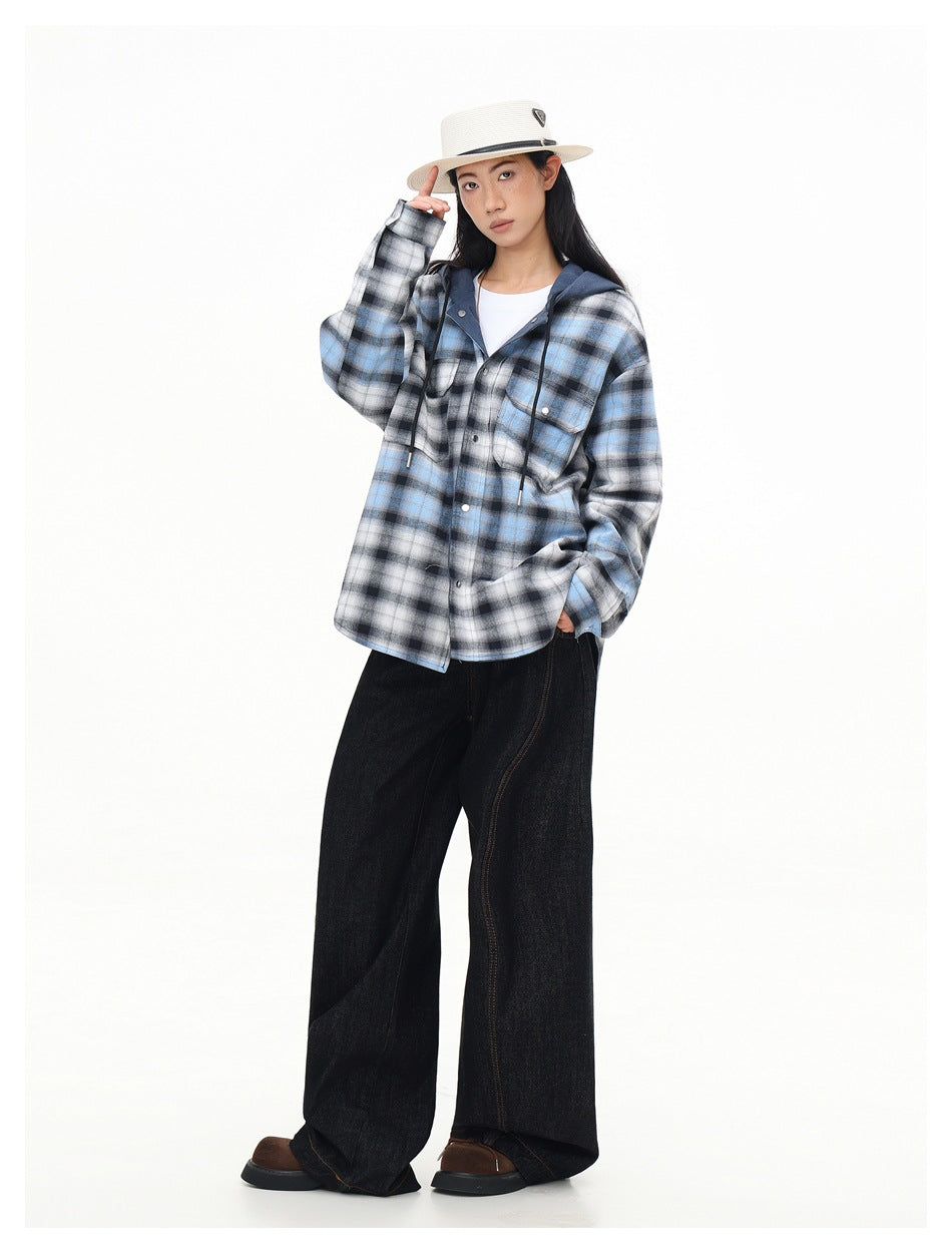 Model wearing a blue, black, and white plaid hooded button-up shirt over a white tee, with wide black jeans.