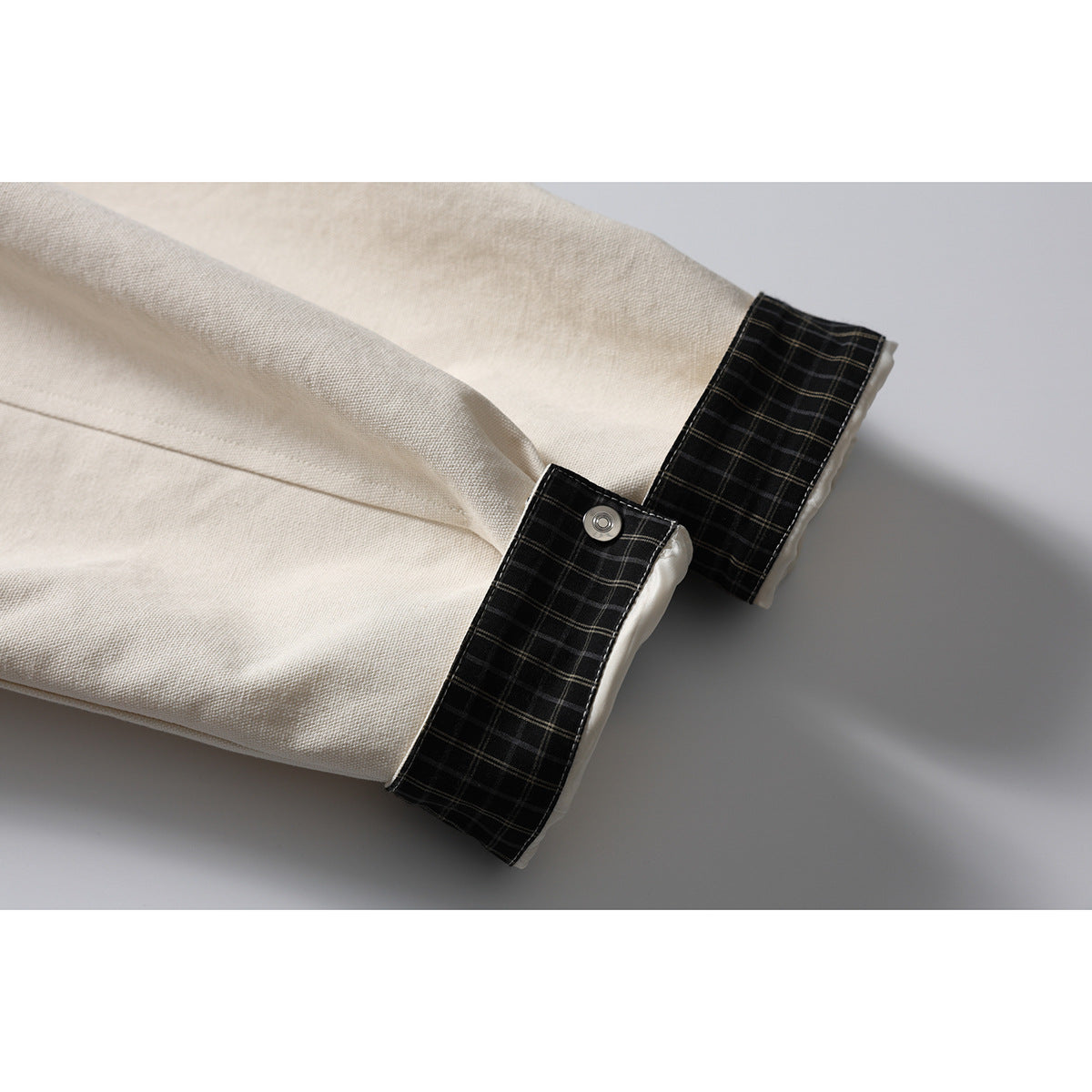 Close-up of an ivory jacket cuff with dark plaid trim and a metal snap.