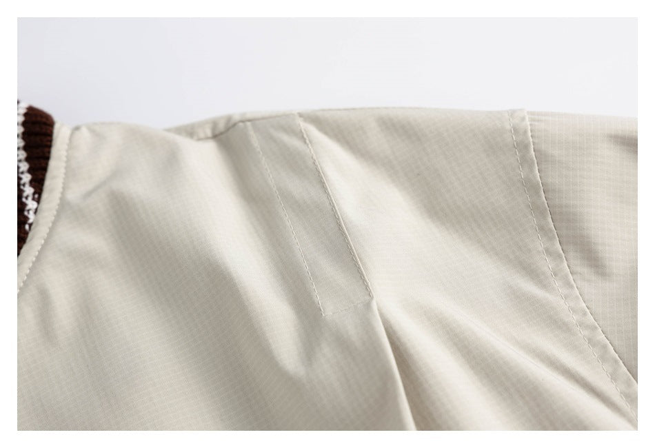 Close-up of cream jacket fabric and stitched panel seams near the brown-and-cream ribbed trim.