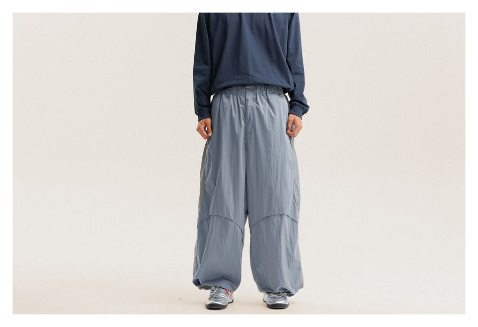 Front view of a model wearing oversized slate-blue pants with a button waist, curved panel seams, and gathered cuffs.