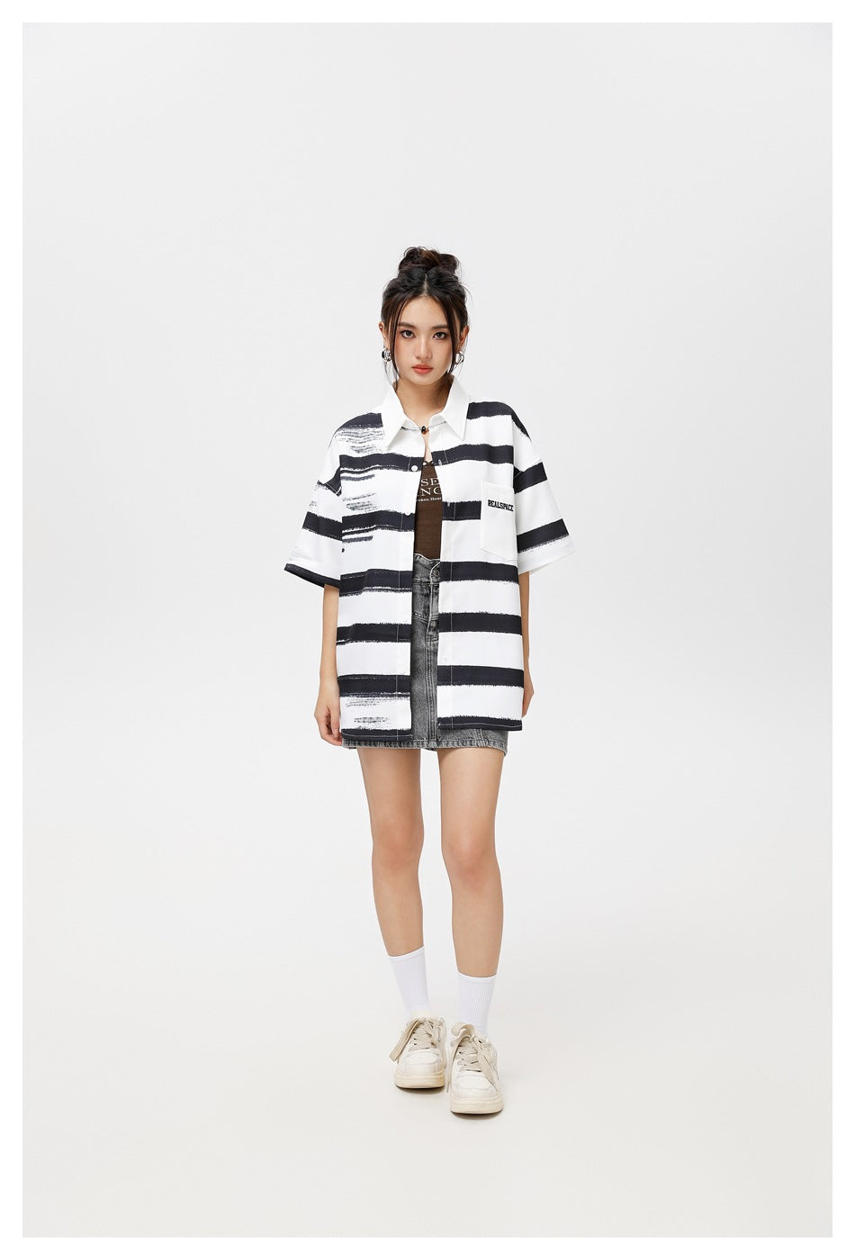 Full-length model wearing a white shirt with black brushstroke stripes, layered over a gray denim mini skirt.