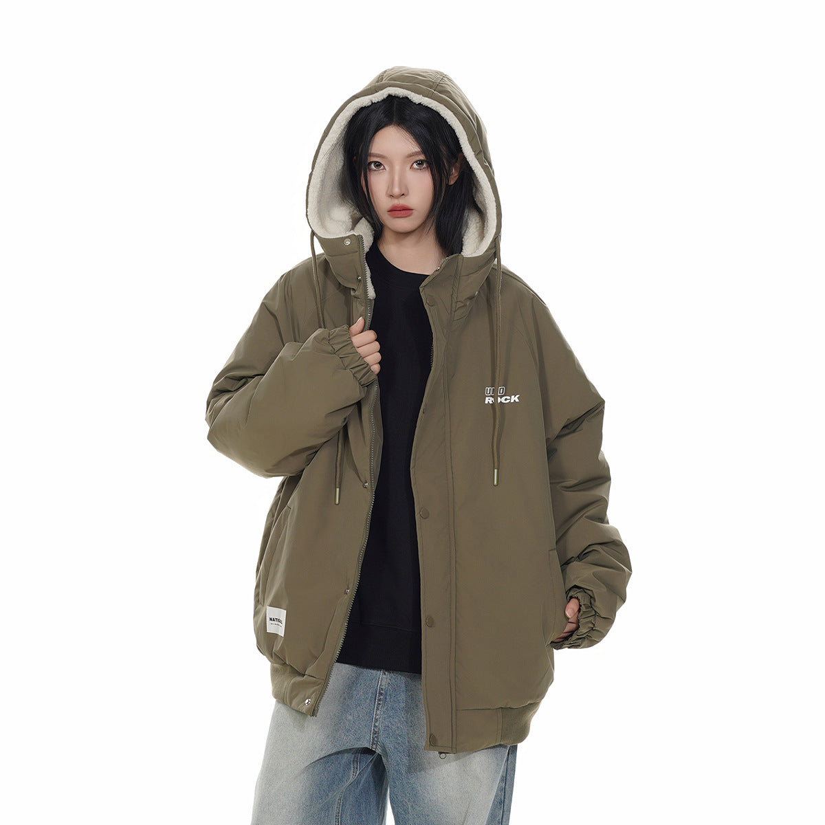 Closer front view of a model wearing an olive hooded jacket with cream fleece lining and a black top.