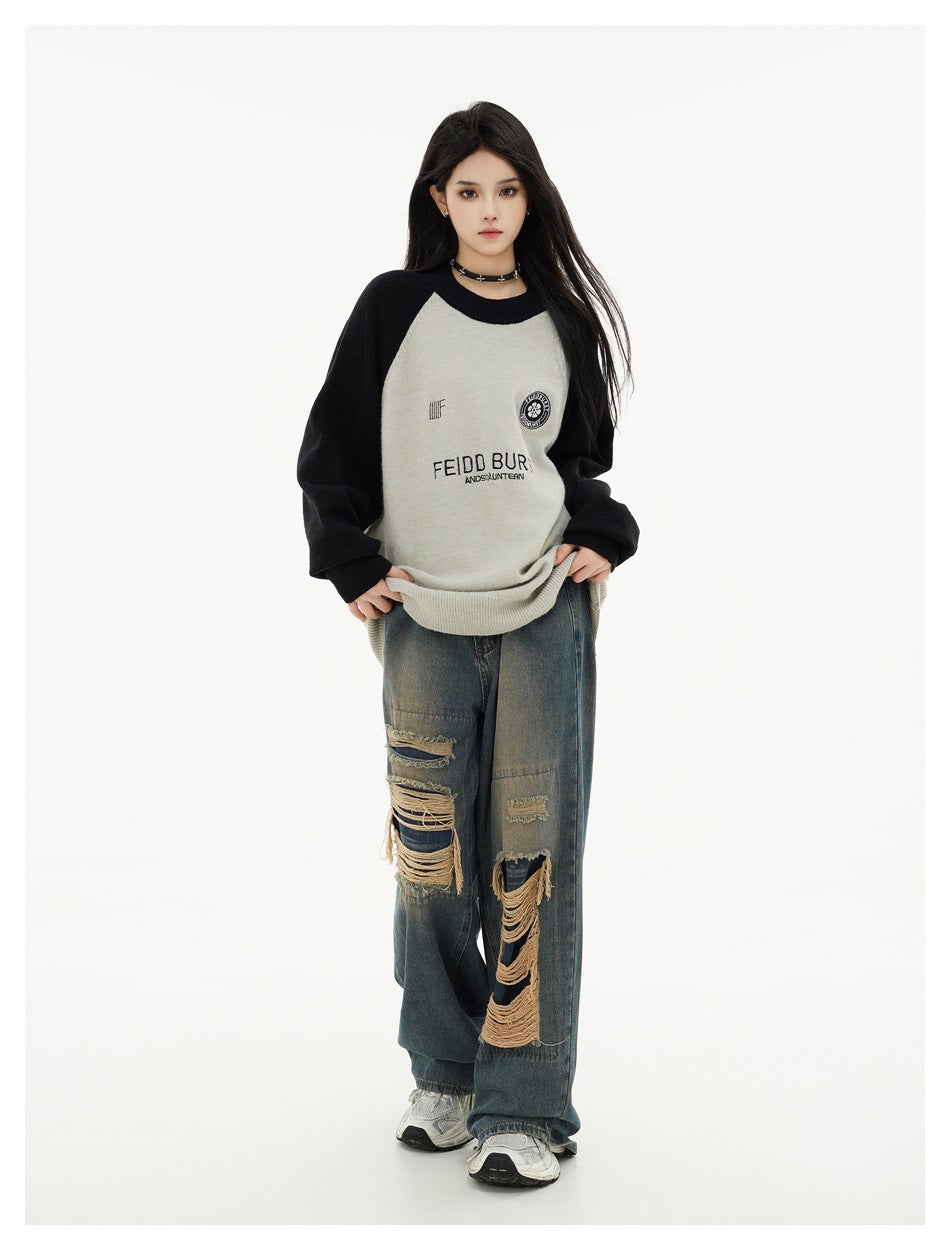 Full-length front view of a model wearing a light gray sweater with black raglan sleeves and distressed wide-leg jeans.
