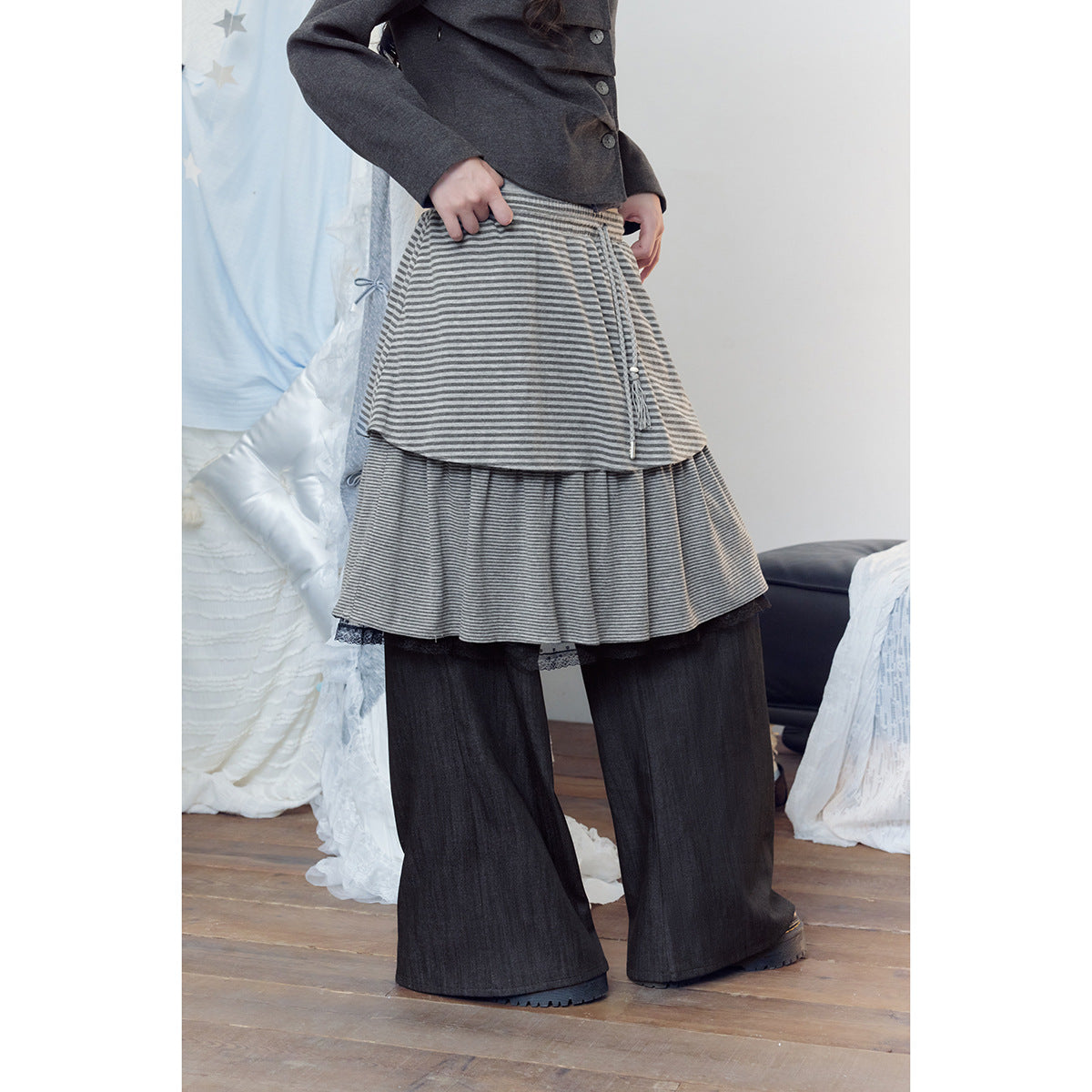 Cropped model wearing a gray striped layered skirt over wide charcoal pants, with a dark buttoned jacket.
