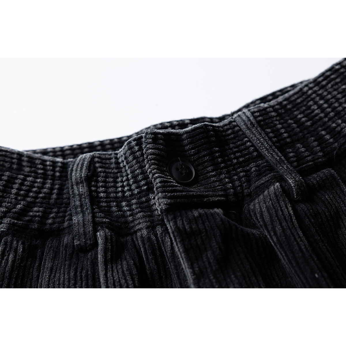 Close-up of black ribbed trousers showing the buttoned waistband, belt loops and front pleats.