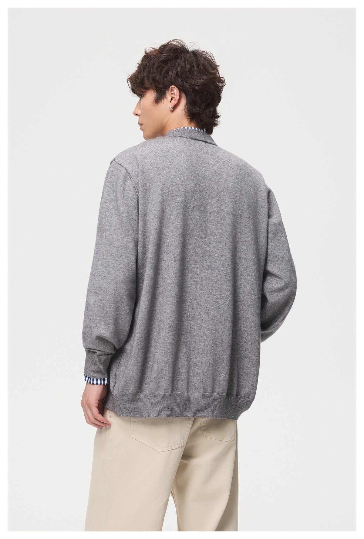 Rear view of a model wearing a gray cardigan with ribbed cuffs and hem over cream trousers.