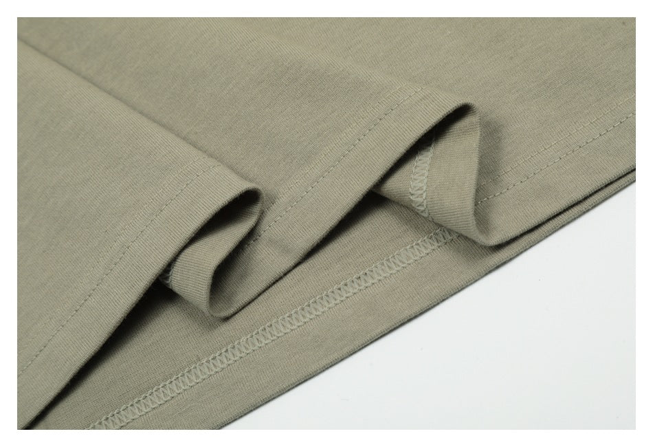 Close-up of a muted olive-gray garment hem showing folded fabric and overlock stitching.