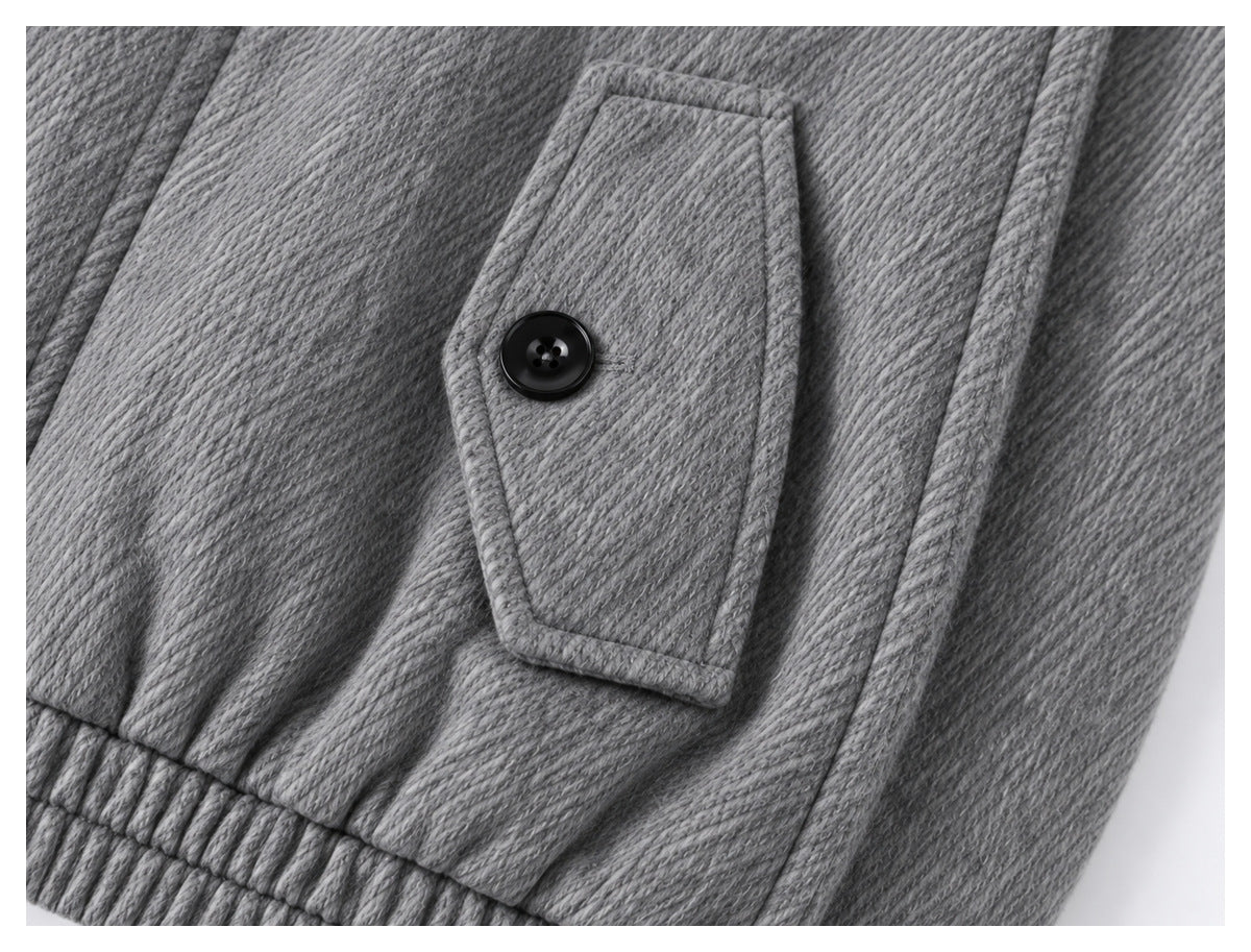 Close-up of a buttoned flap pocket, textured gray fabric and gathered hem on the jacket.