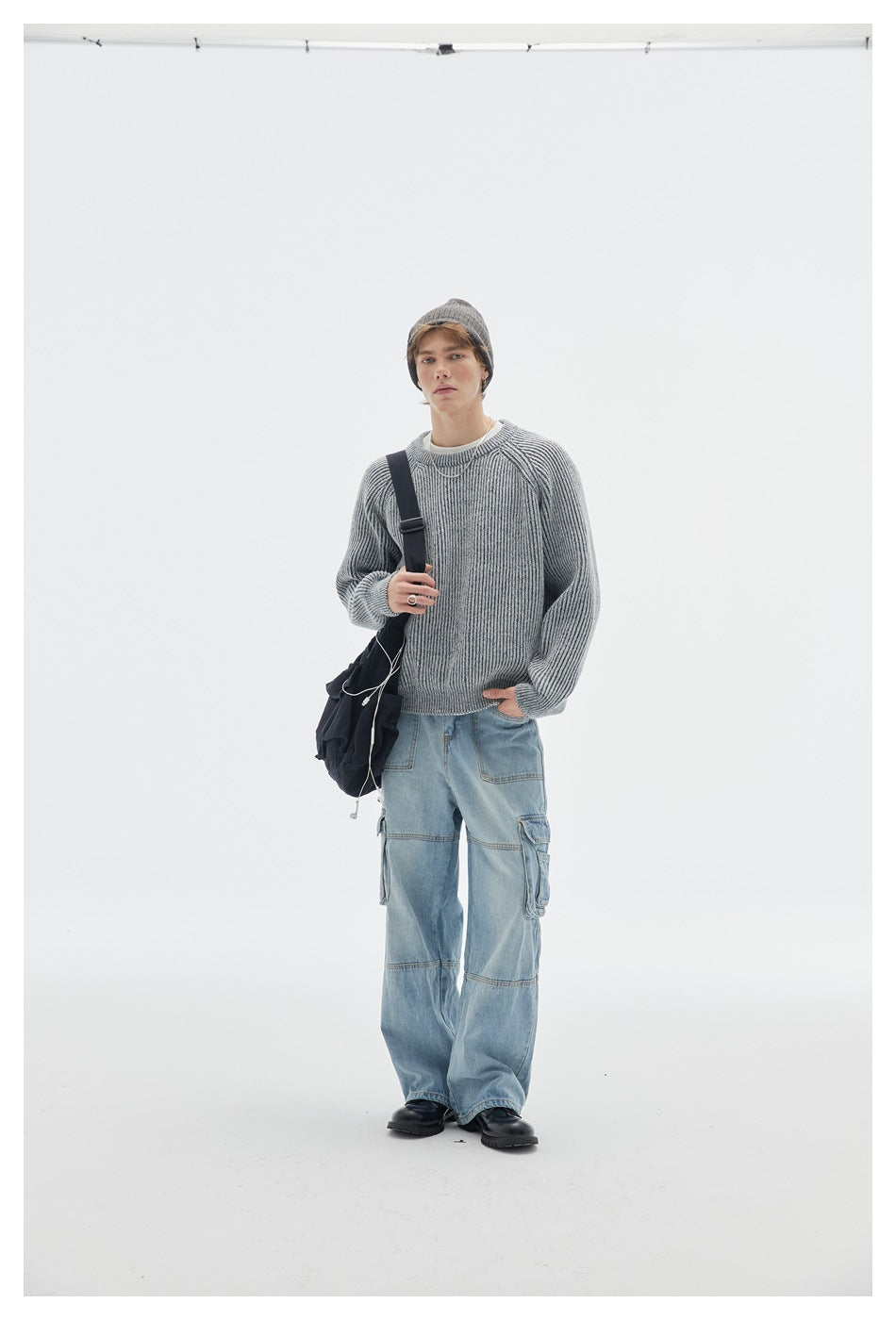 Front view of a model in a light gray ribbed raglan sweater with cargo jeans, beanie and a black crossbody bag