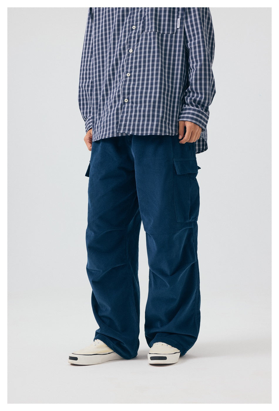 Front view of a model wearing loose navy cargo pants with flap pockets and a blue plaid shirt.