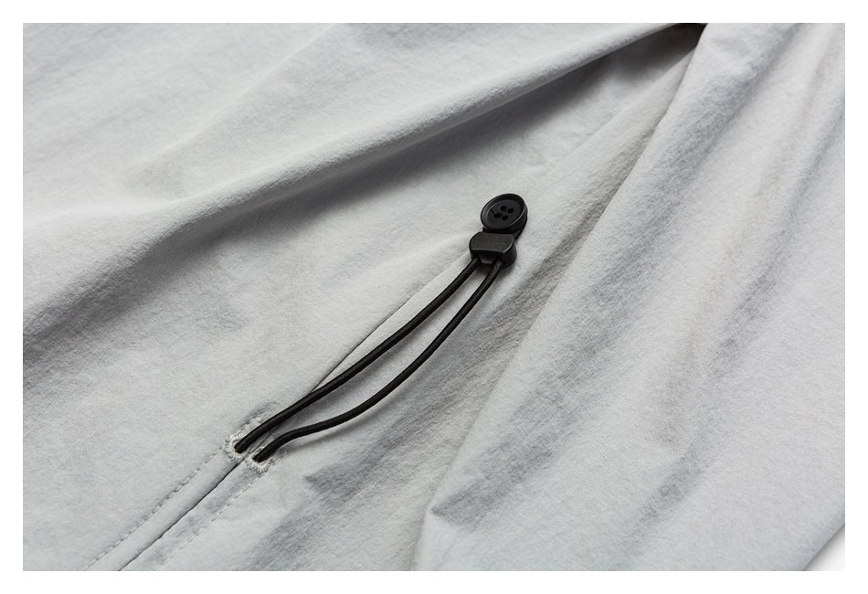 Close-up of a black drawcord and button detail against light gray shorts fabric.