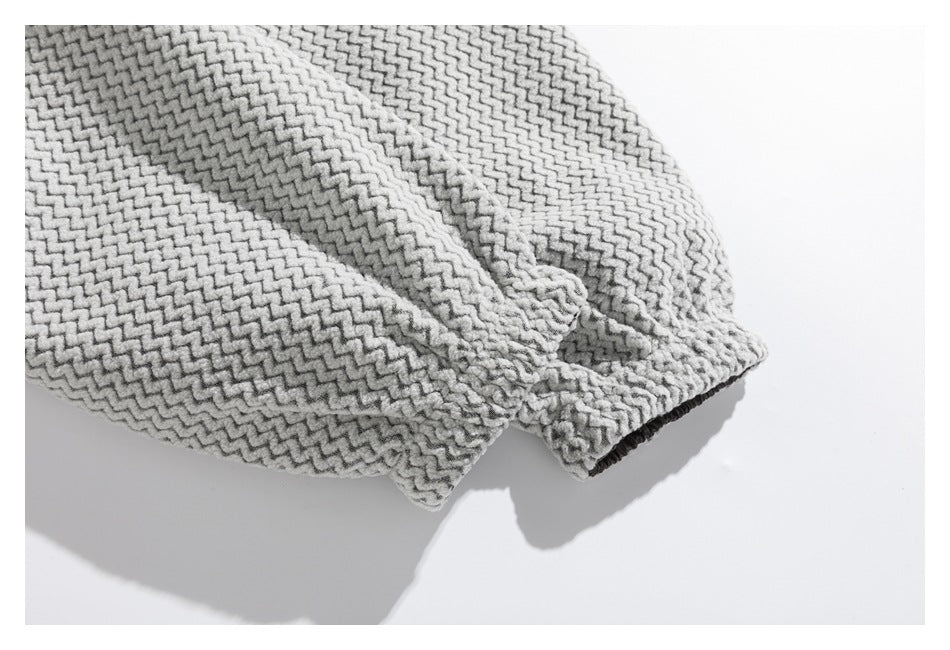 Close-up of a light gray garment sleeve with a raised zigzag texture and dark ribbed cuff.
