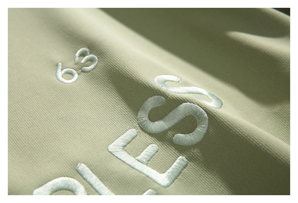 Angled close-up of white embroidered lettering on pale sage-green sweatshirt fabric.