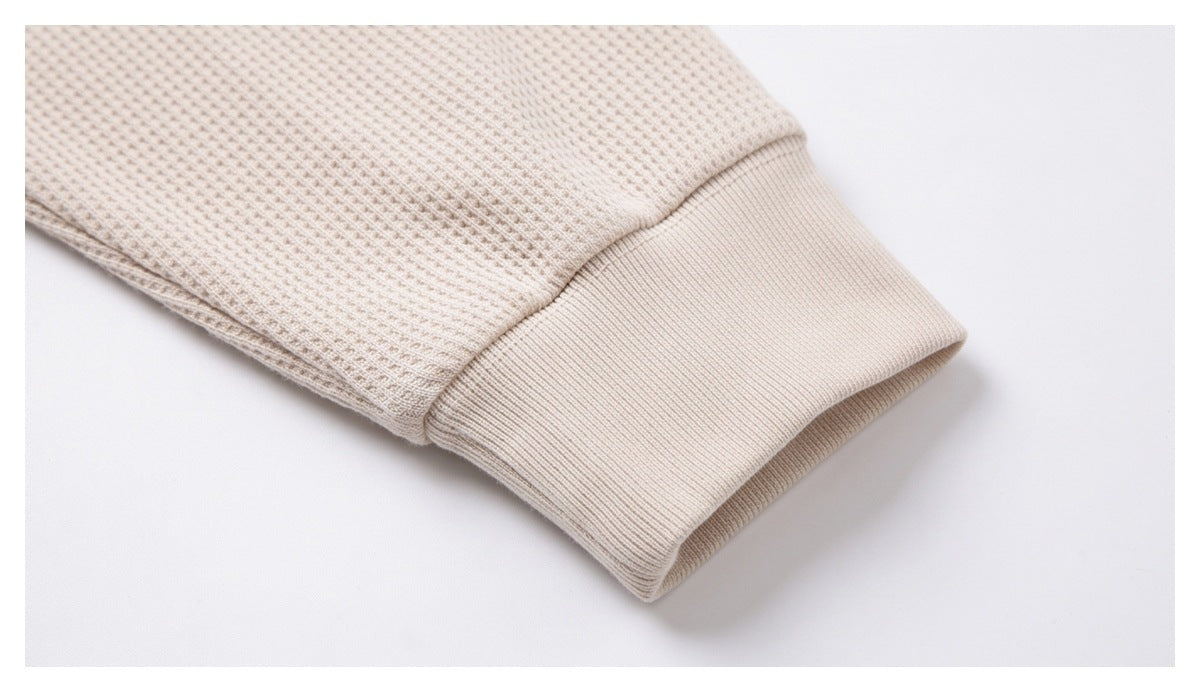 Close-up of a cream waffle-knit sleeve ending in a wide ribbed cuff.