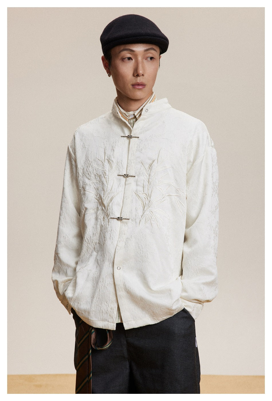 Model wearing an ivory stand-collar jacket with tonal bamboo embroidery and metal frog closures.