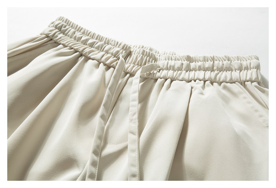 Close-up of ivory pants showing the gathered elastic waistband, drawstring, and front pocket opening.