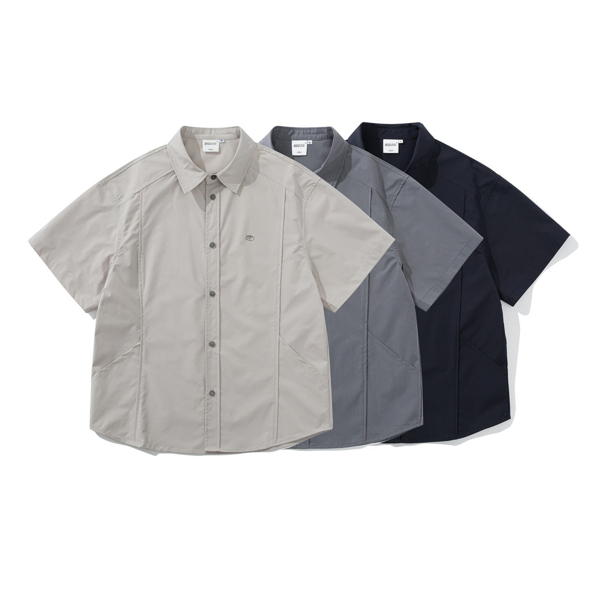 Three short-sleeve button-up shirts displayed together in light beige, gray, and dark navy.