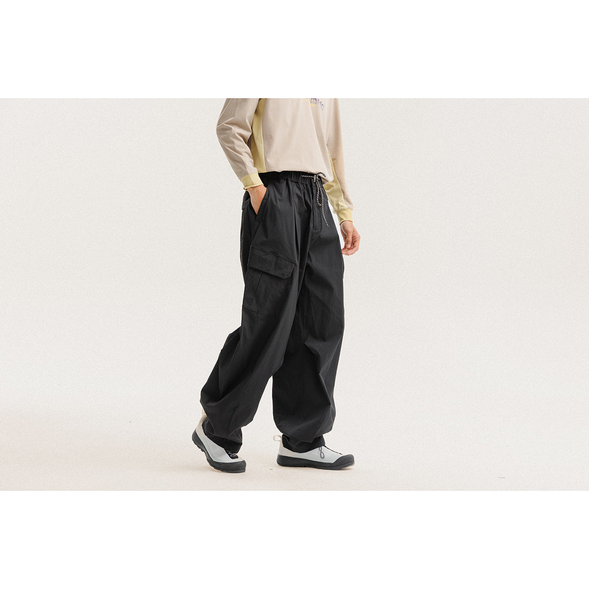 Model wearing loose black cargo pants with a drawstring waist and large flap pockets, shown from the side.
