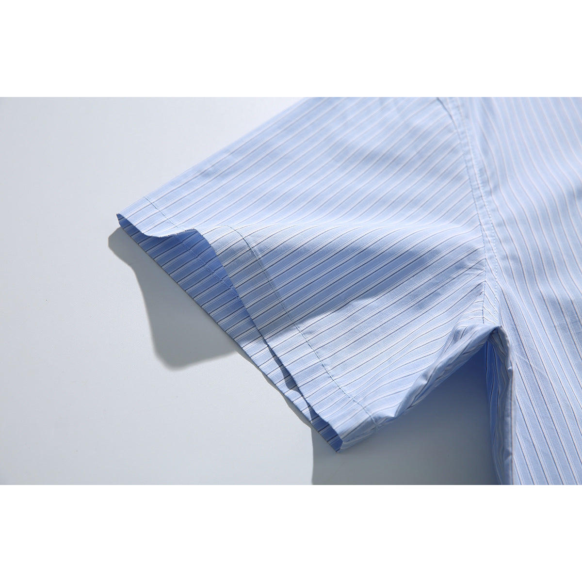 Close-up of the short sleeve and stitched hem of a light blue striped shirt.