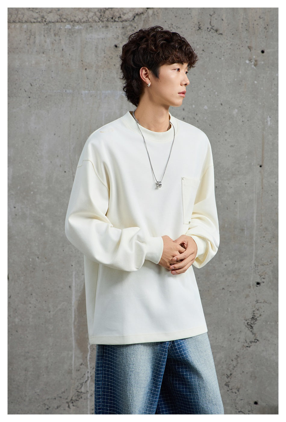 Model wearing an oversized ivory crewneck sweatshirt with a large chest pocket and ribbed cuffs.