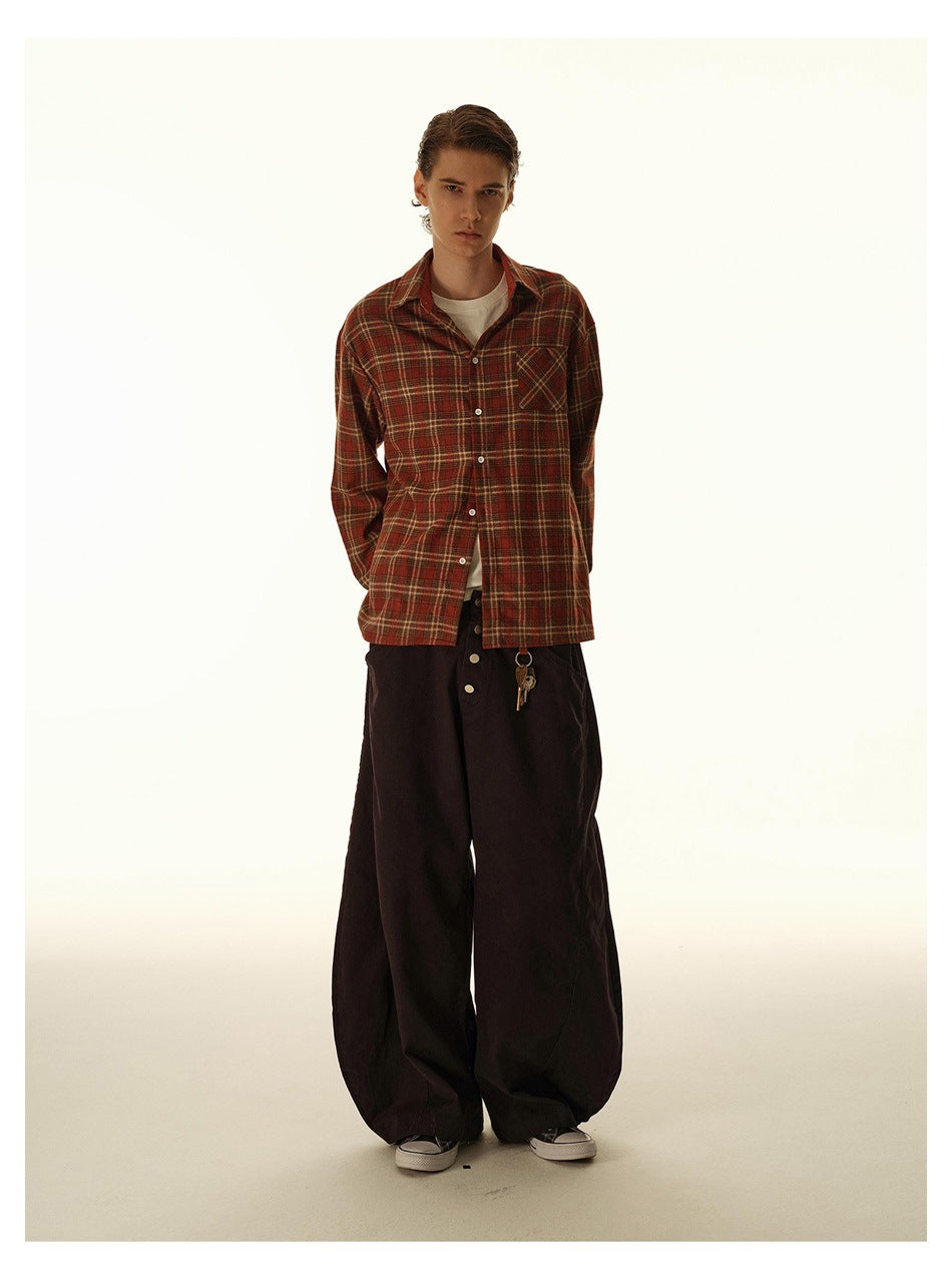 Full-length view of a model in a red plaid button-up shirt over a white tee with wide dark trousers