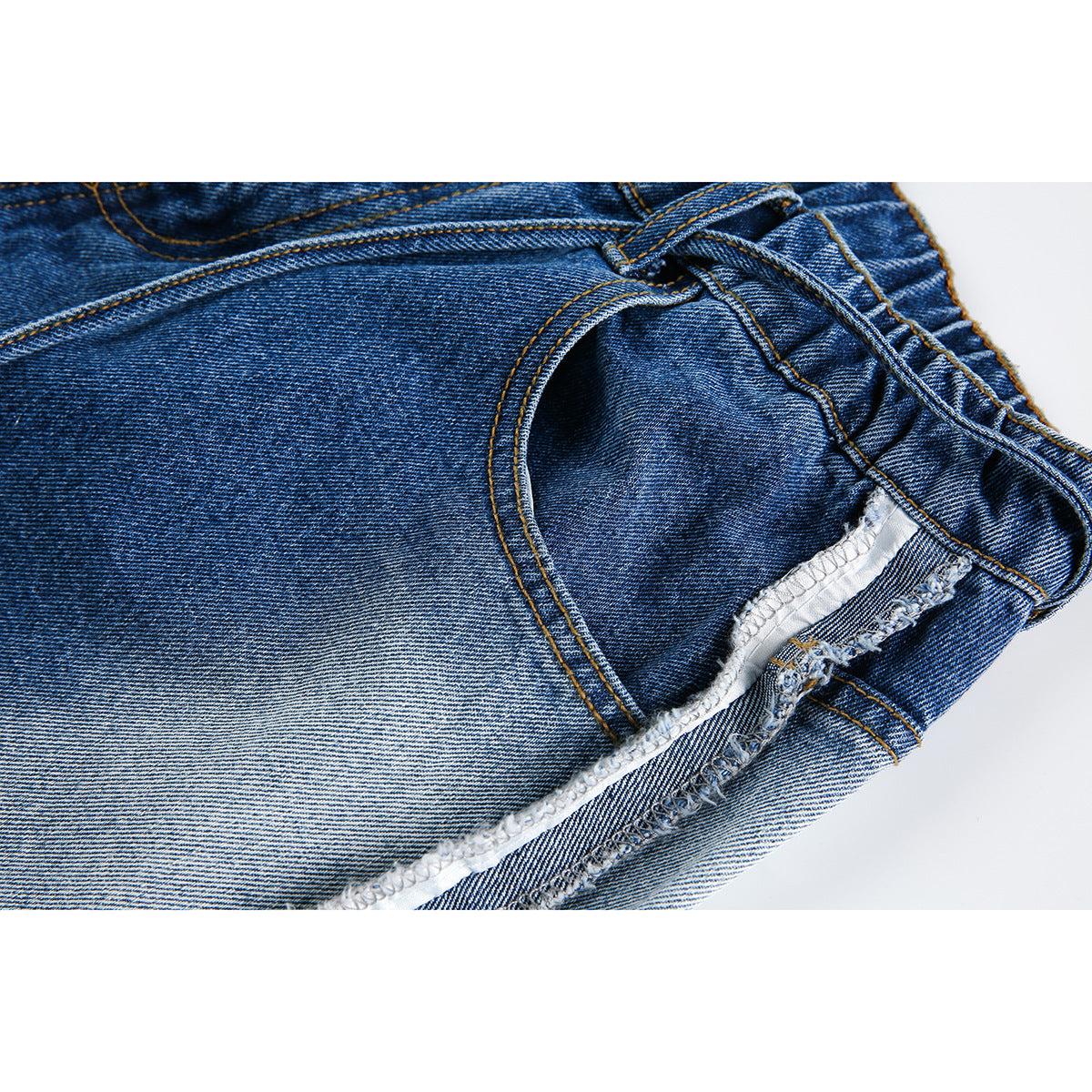 Close-up of blue denim shorts showing a front pocket, waistband stitching, and a frayed exposed side seam.