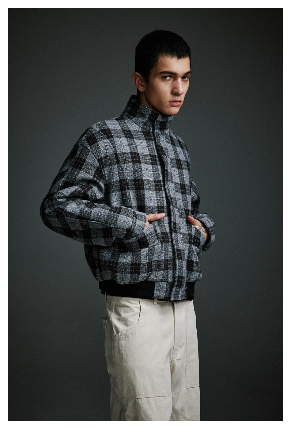 Man wearing a gray and black plaid jacket with hands in its pockets and cream cargo pants.